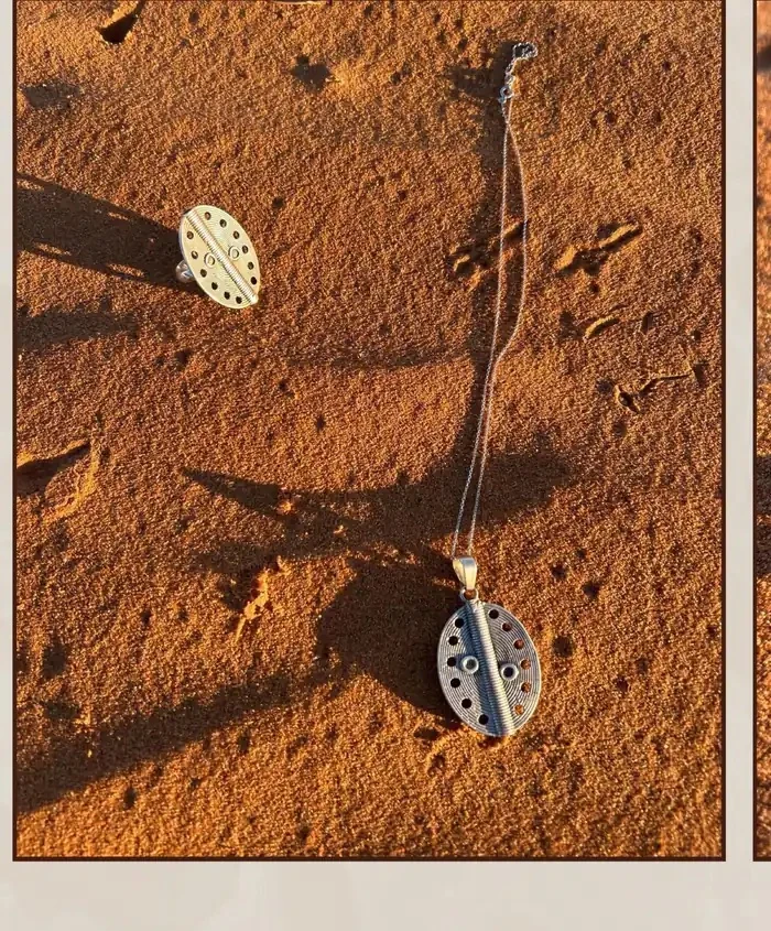 Détails de pendentifs SYKA présentés sur le sable.